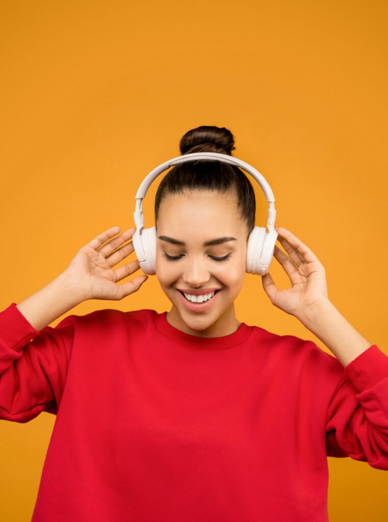 pexels-photo-3756770-3756770 Young woman smiling and listening to music with headphones against orange background.